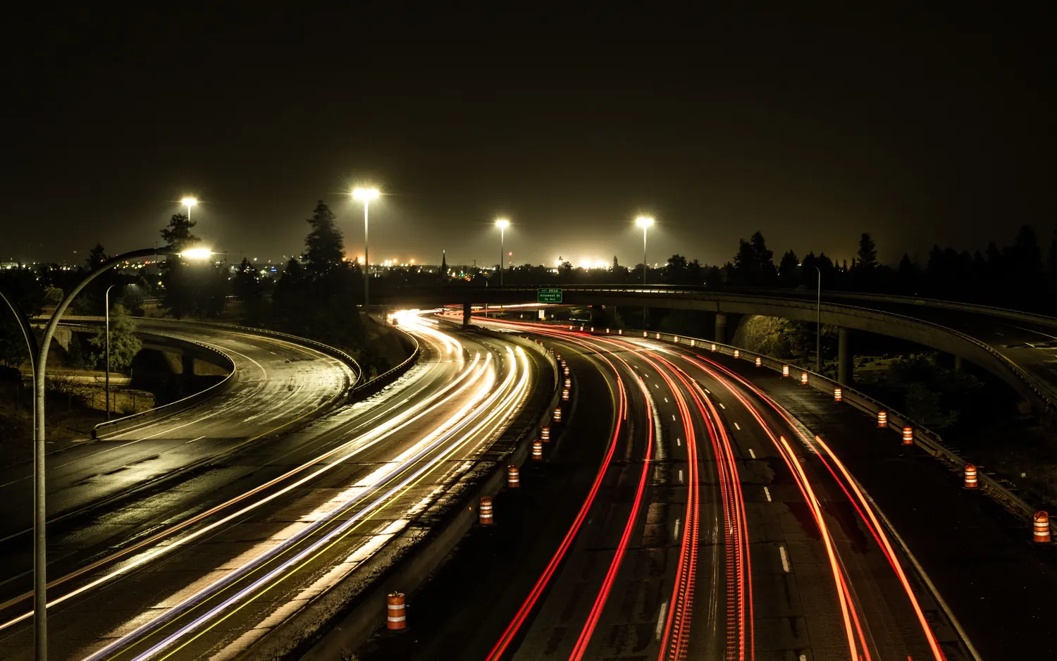 Rastros de luz de dois fluxos de veículos que convergem em uma rodovia à noite.